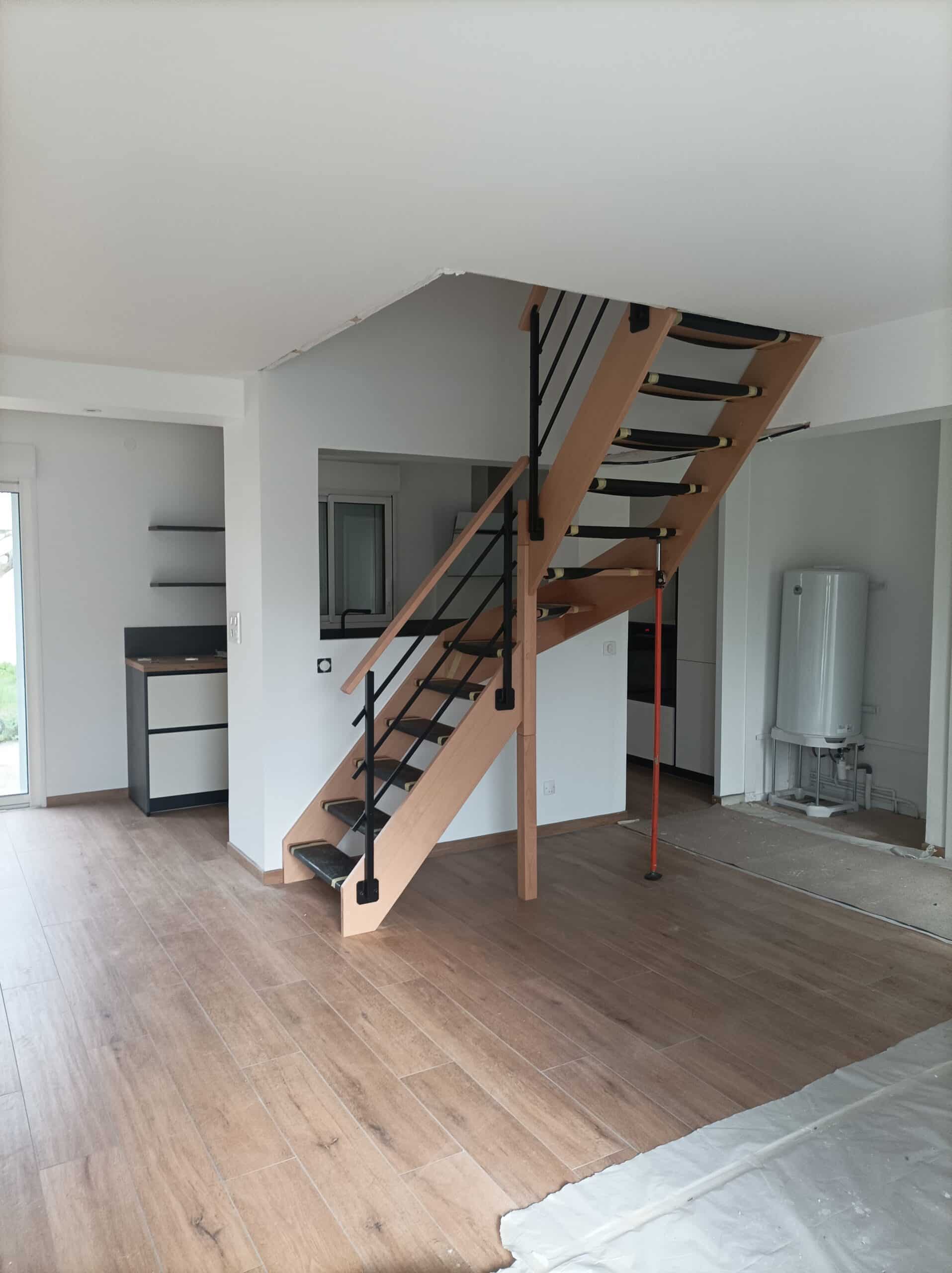 Escalier intérieur moderne en bois clair avec rampe noire, dans une pièce en cours de finition avec sol carrelé imitation bois.
